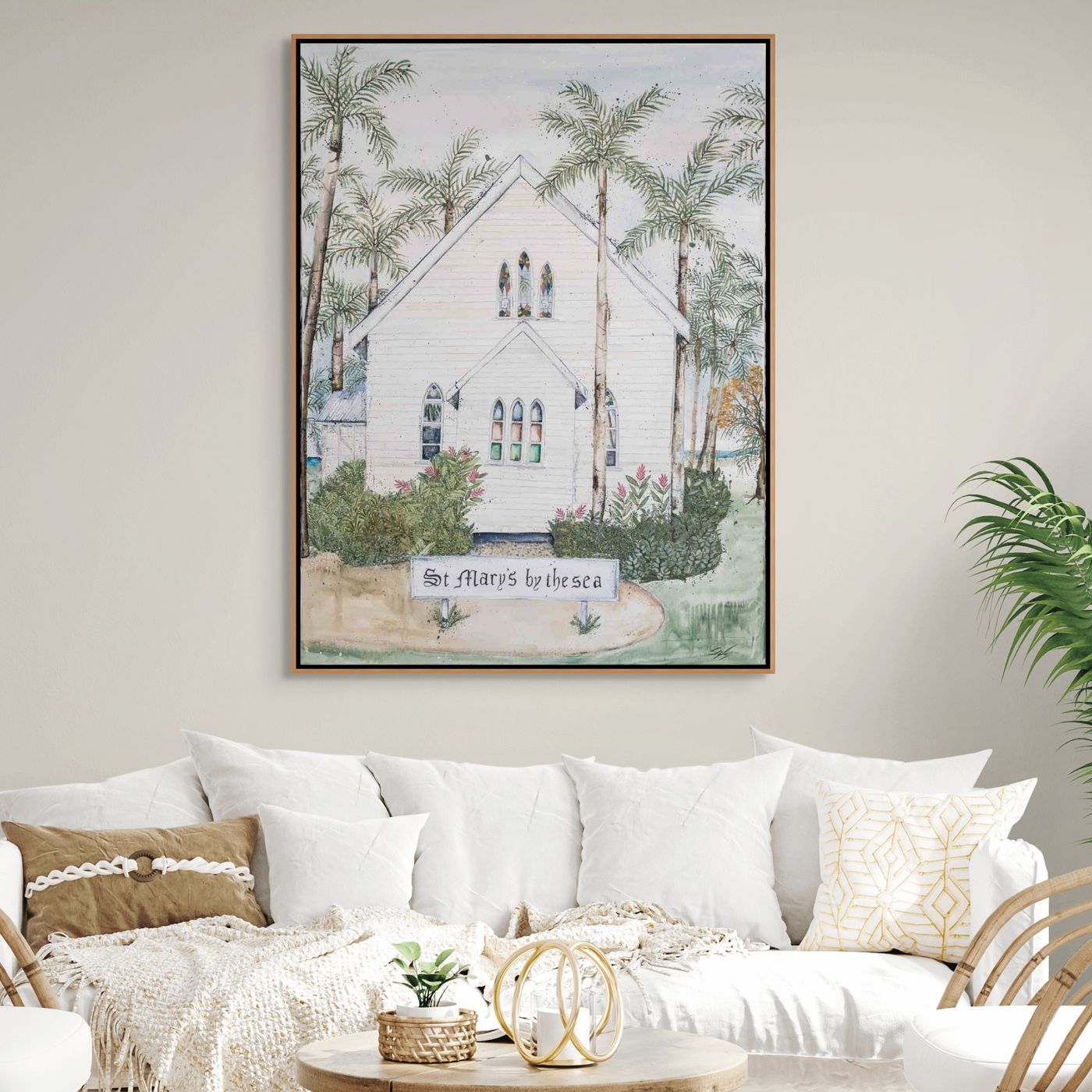 Framed artwork of a beach scene with a house and palm trees above a white sofa.